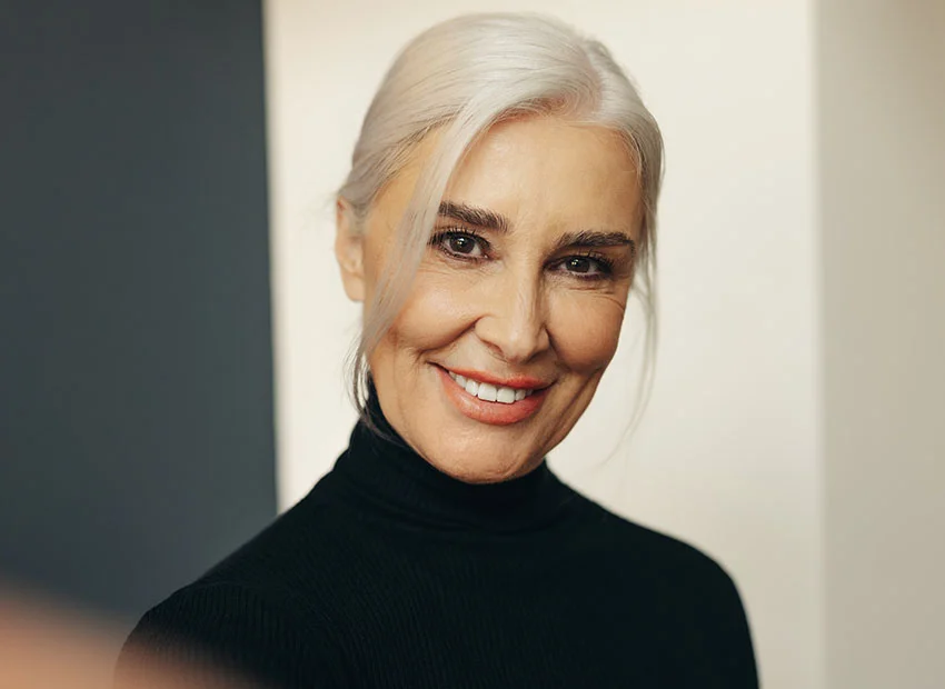 A senior woman with white hair tied back, wearing a black turtleneck, smiling warmly - All on 4 Procedure in Boca Raton, FL